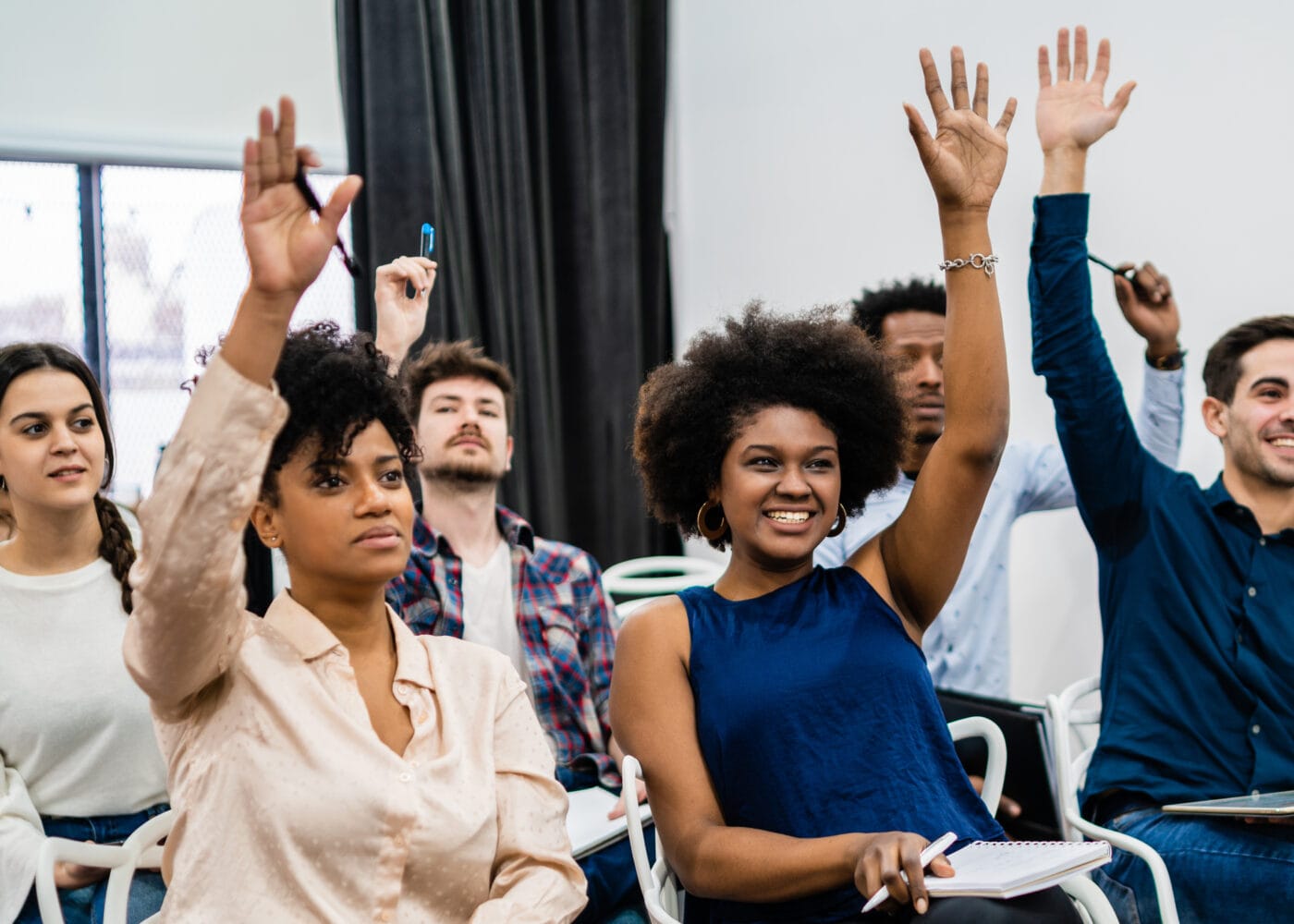 Group of young people sitting on conference together while raising their hands to ask a question. Business team meeting seminar training concept.